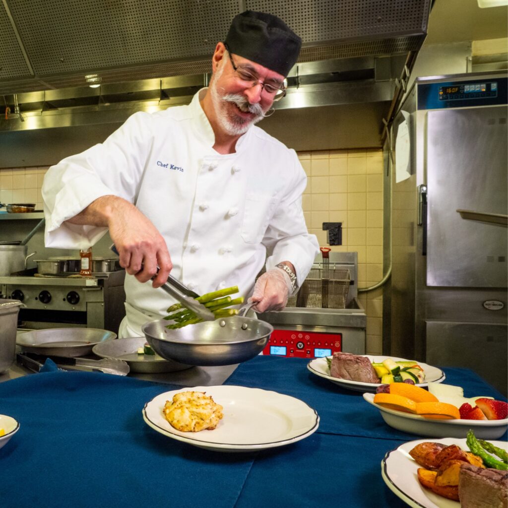 A chef in one of LSMMD's communities adding asparagus to a crab cake dinner meal.